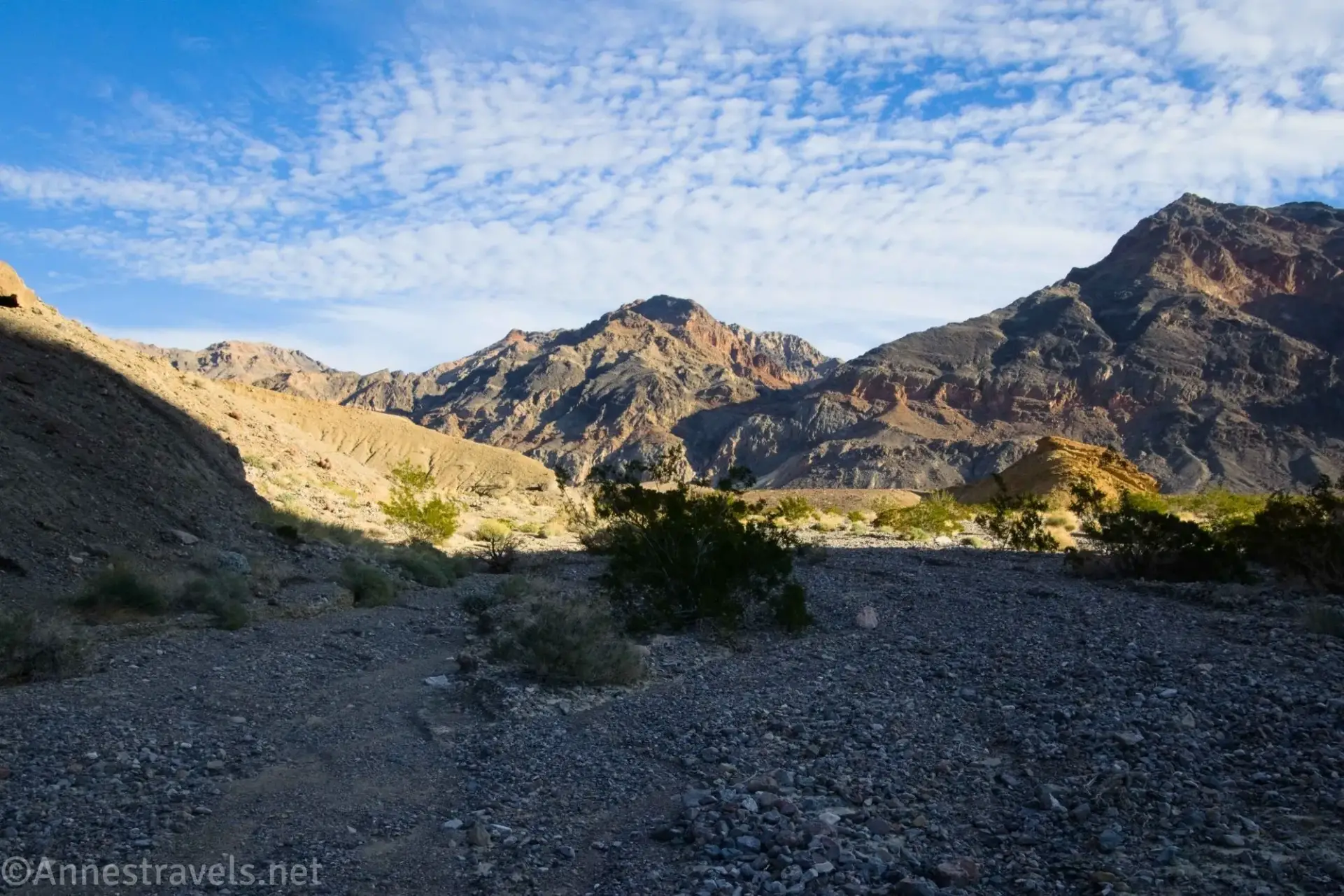 Slit Canyon Wash Shadows in a gravel wash with sunshine on distant desert mountains below blue skies with clouds