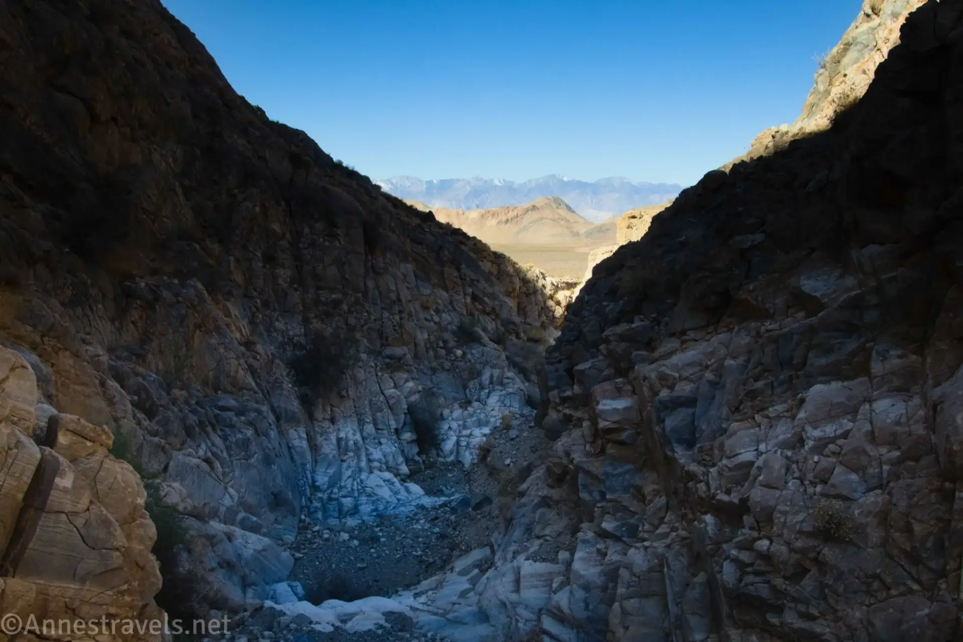 Views down Ubehebe Canyon A rocky, shadowed gorge gives way to dry and snowy mountains across the plain