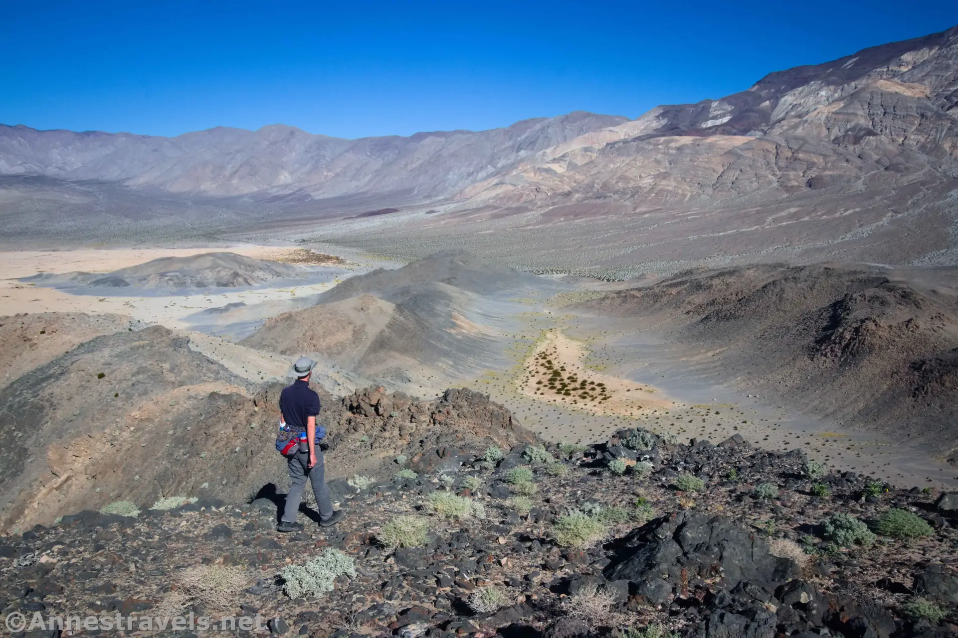 Hiking down Lake Hill A hiker on a rocky slope looking down at a desert with hills and playa and distant mountains