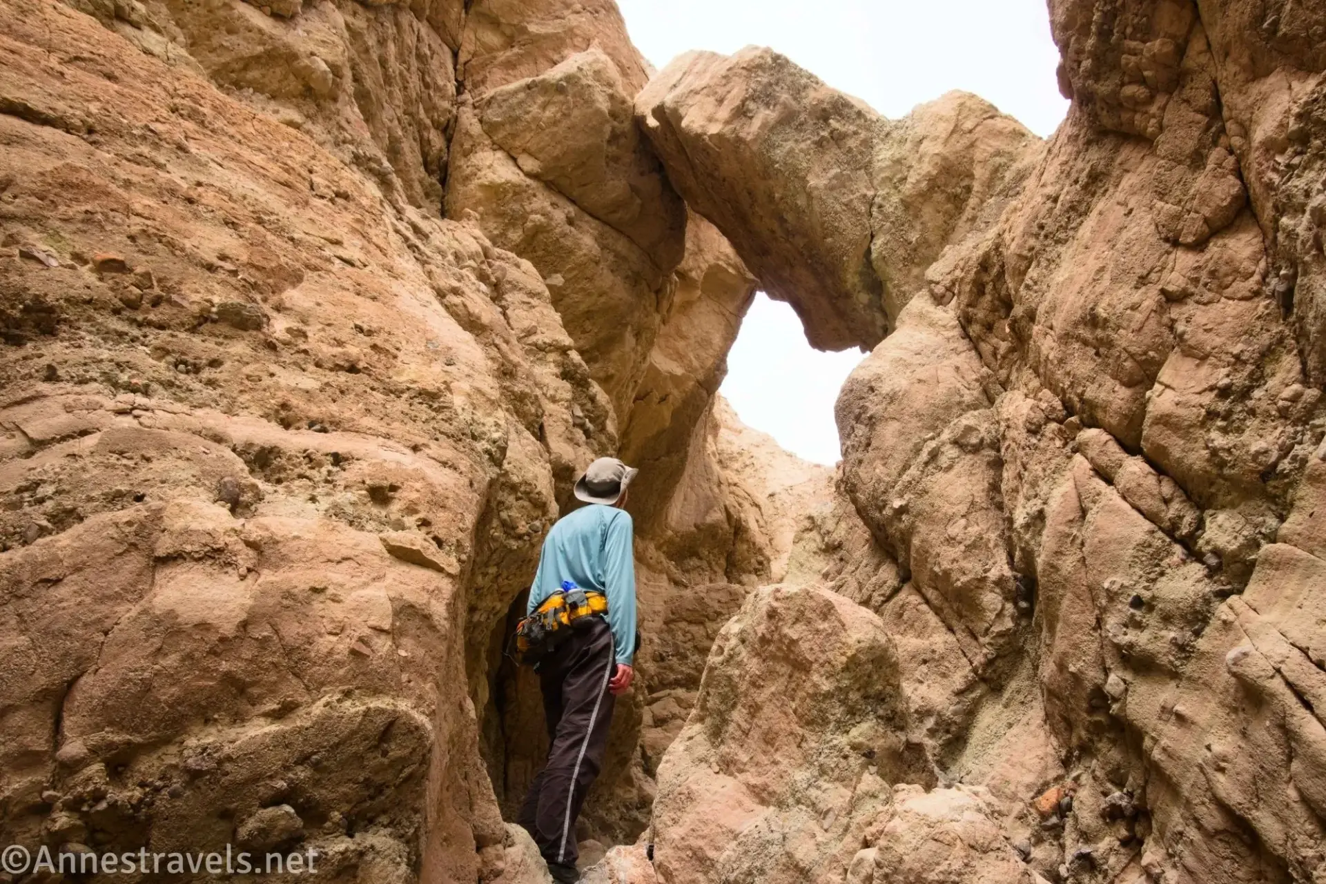 Arch in False Bridges Fork A hiker looks up at a rock overhanging a narrow rock canyon