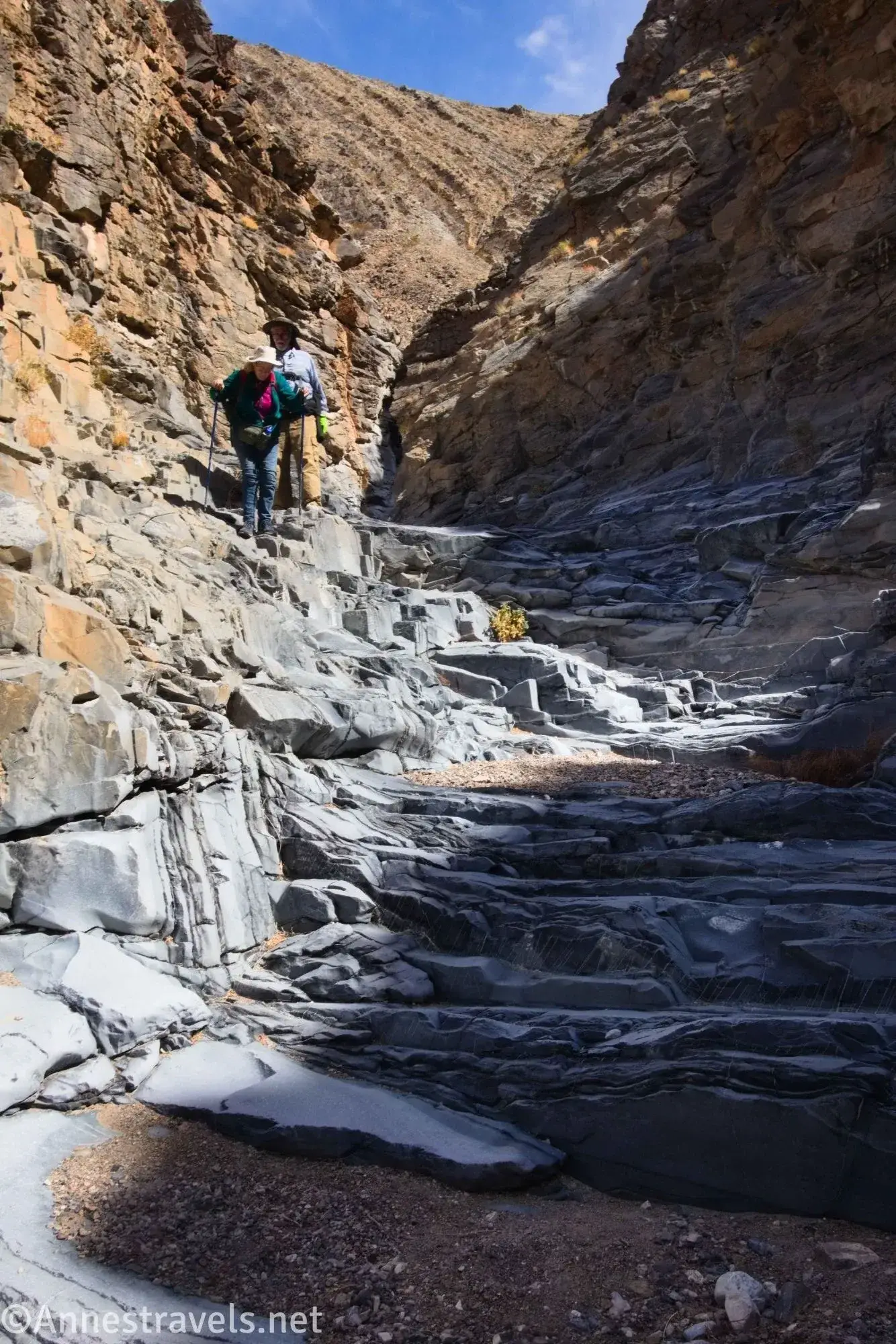 Two hikers climb down a rock step dryfall in a desert canyon