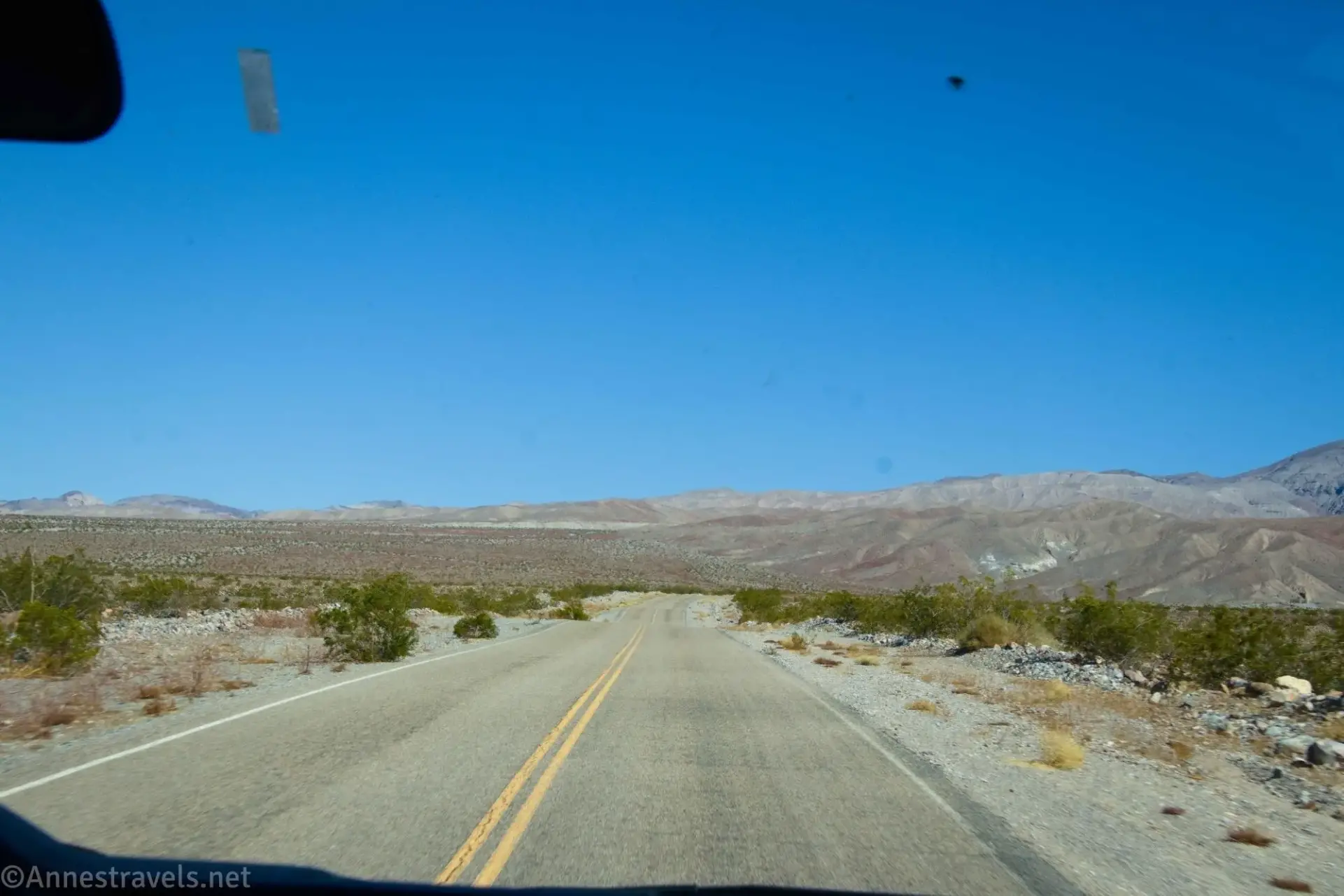 A dusty paved road with a double yellow line down the middle travels across the desert