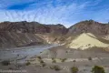 Yellow badlands and brown desert mountains over a gravelly wash