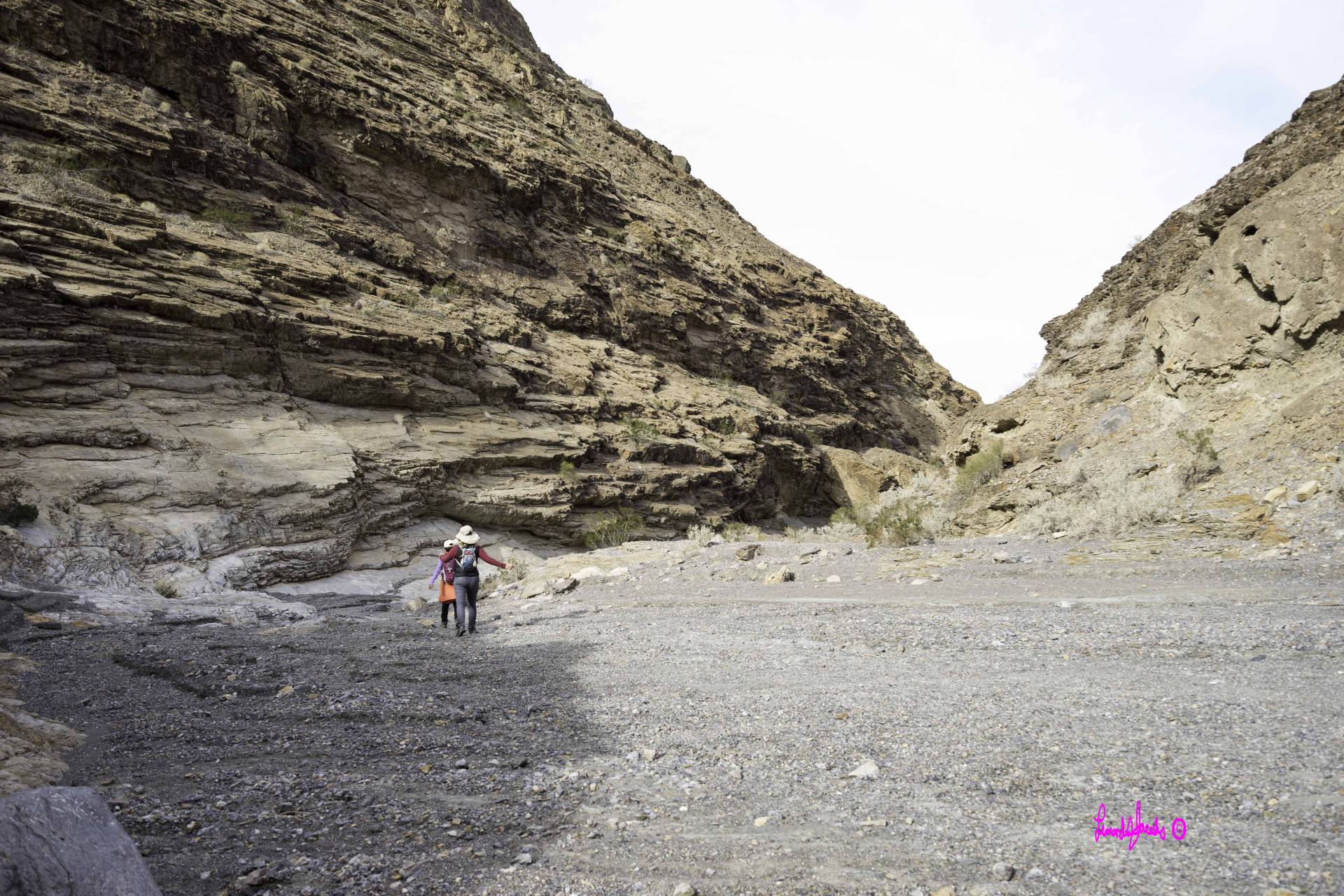 Two hikers in a wide desert canyon with a gravel floor