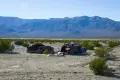 Two old, rusty cars on a brushy desert plain with distant rugged mountains