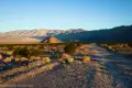 Early morning sunshine on a dirt road, a scrubby desert plain, and desert hills and mountains
