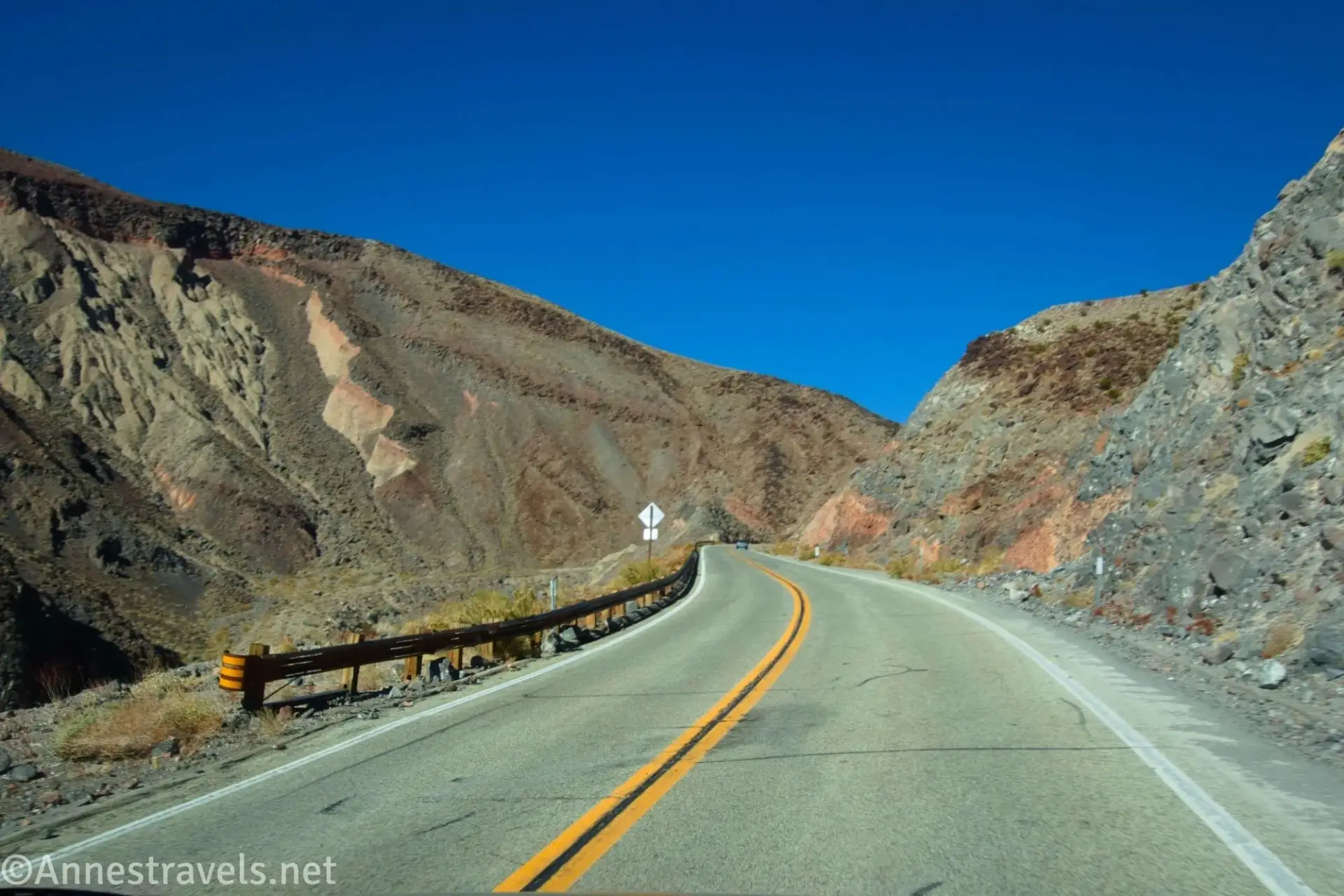 A blacktop road with a guardrail between dirt hills