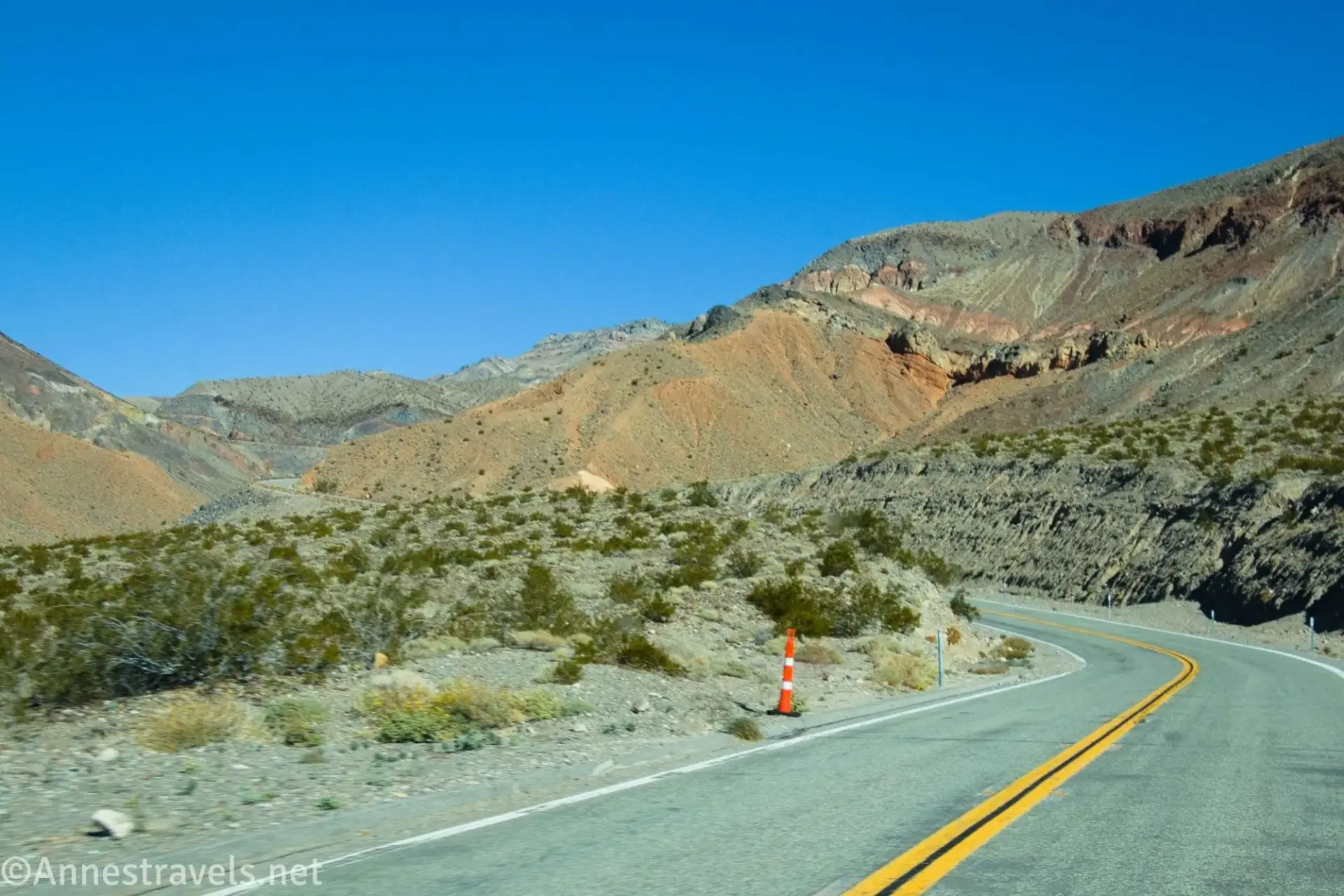 An orange cone beside a road with colorful desert hills in the background