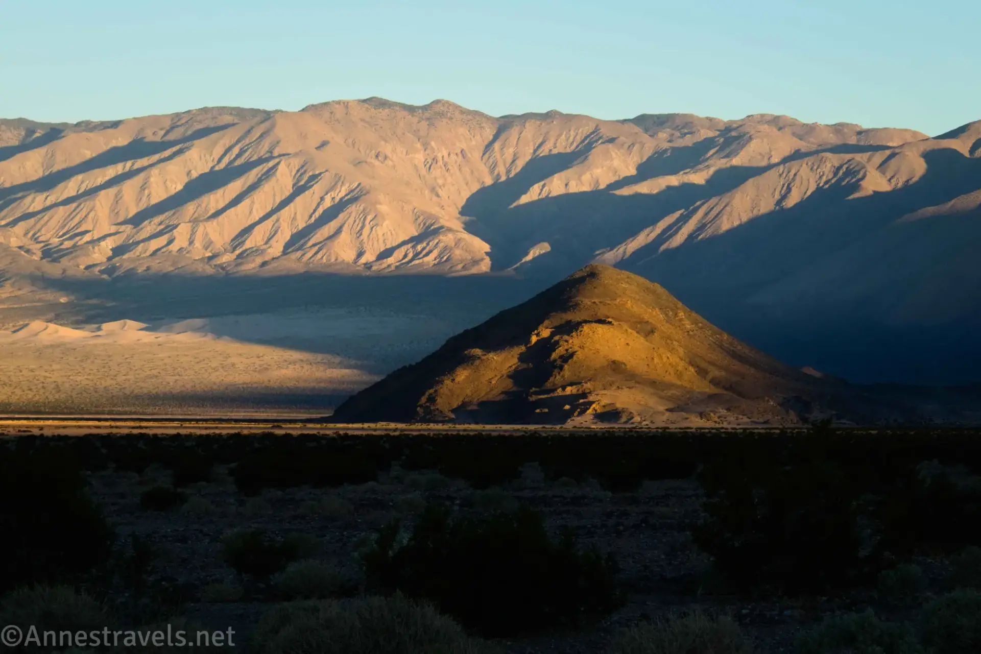 Glow of sun on a nearby brown hill with distant, rugged brown mountains
