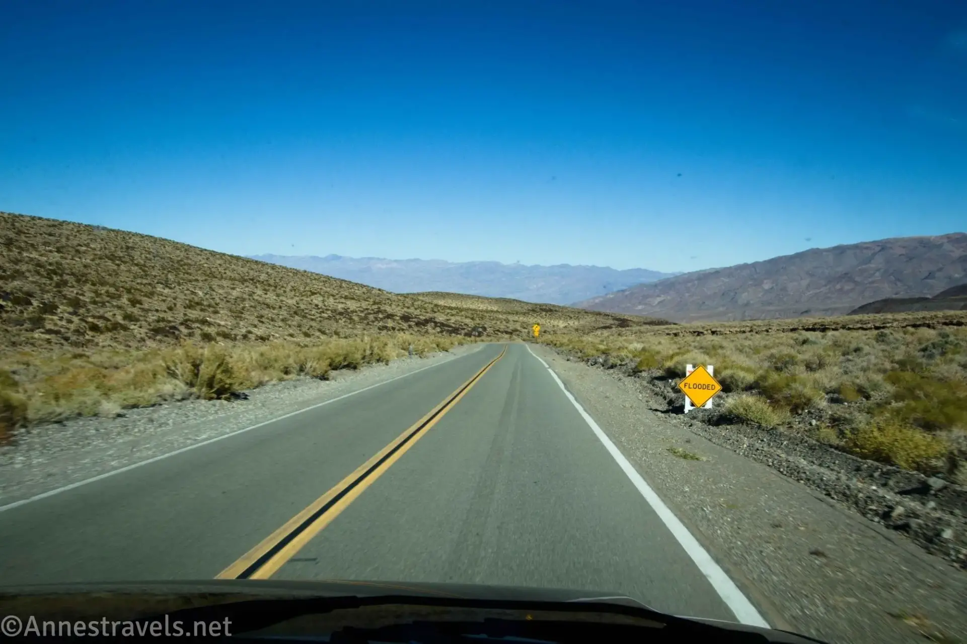 A blacktop road beside a flooded sign in desert mountains