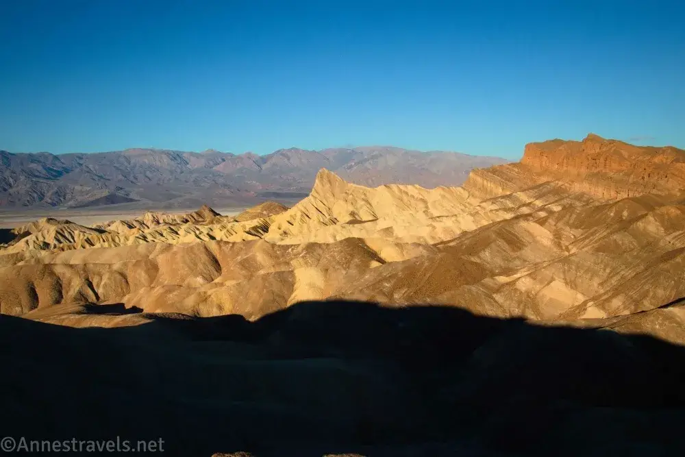 Manly Beacon and striped badlands in front of gray mountains in the early morning light from Zabriskie Point in Death Valley National Park