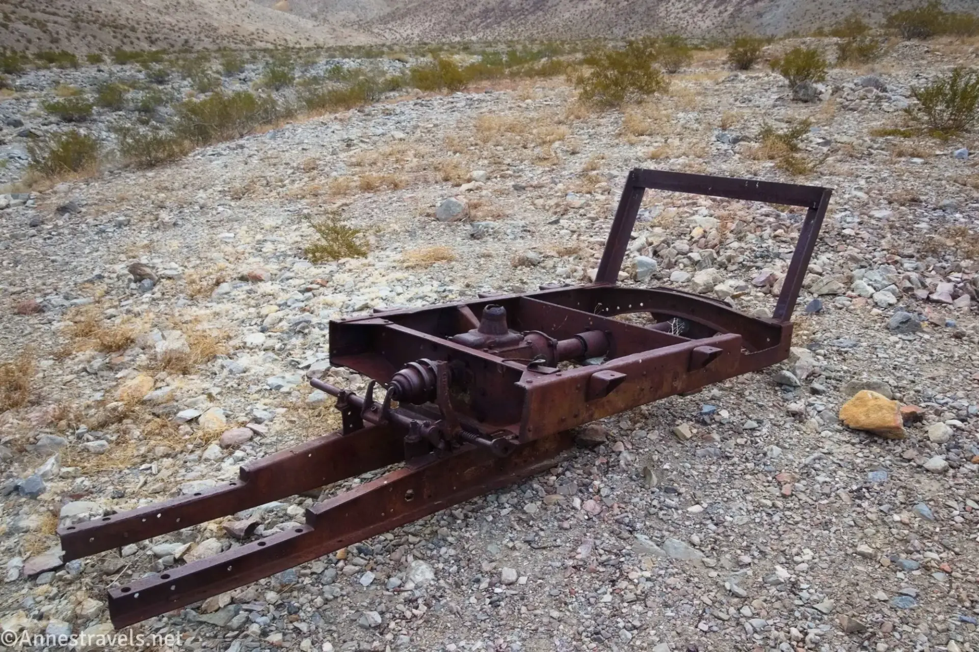 The rusting remains of a vehicle on a gravel surface with desert brush