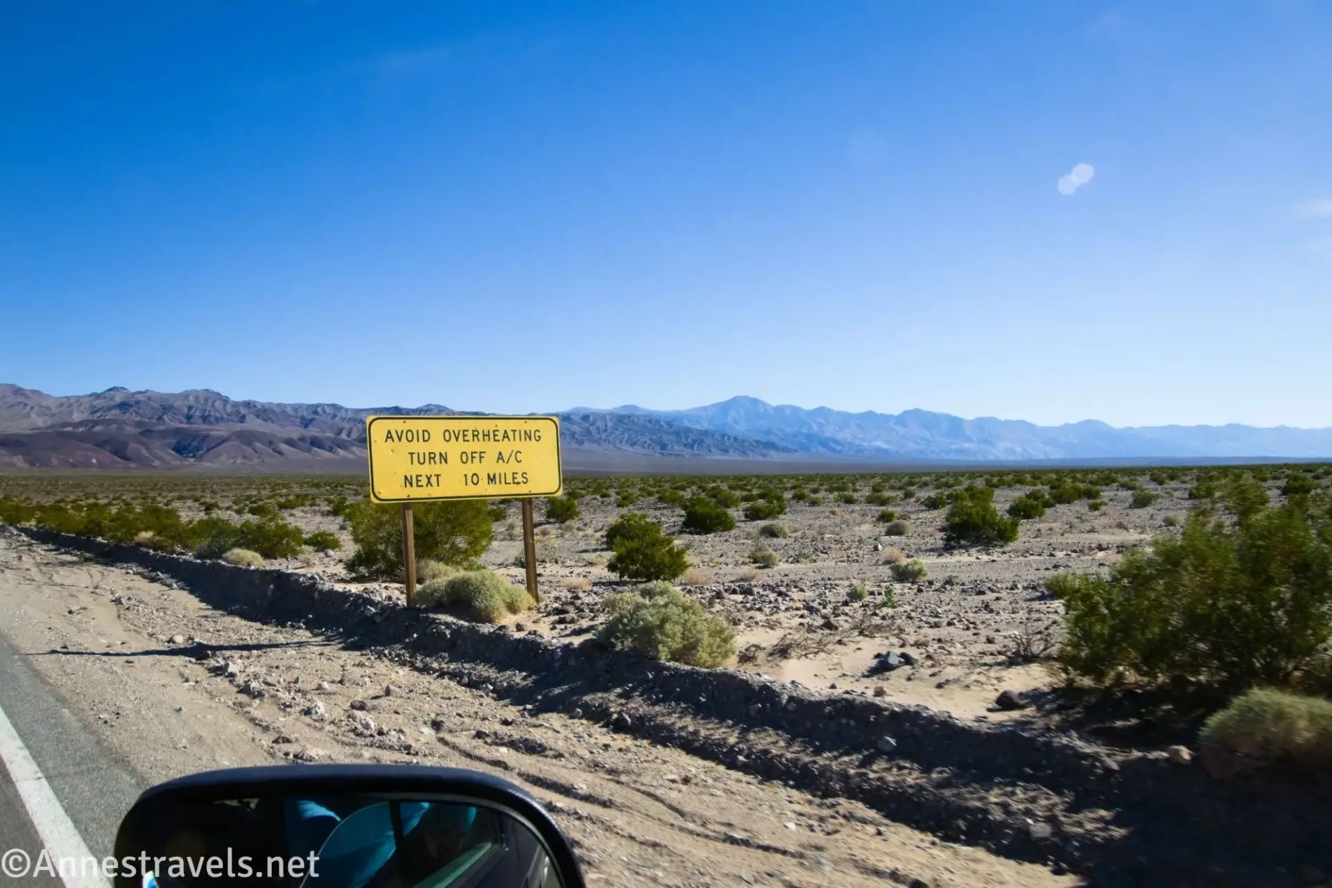 A yellow sign on a desert plain with hazy mountains