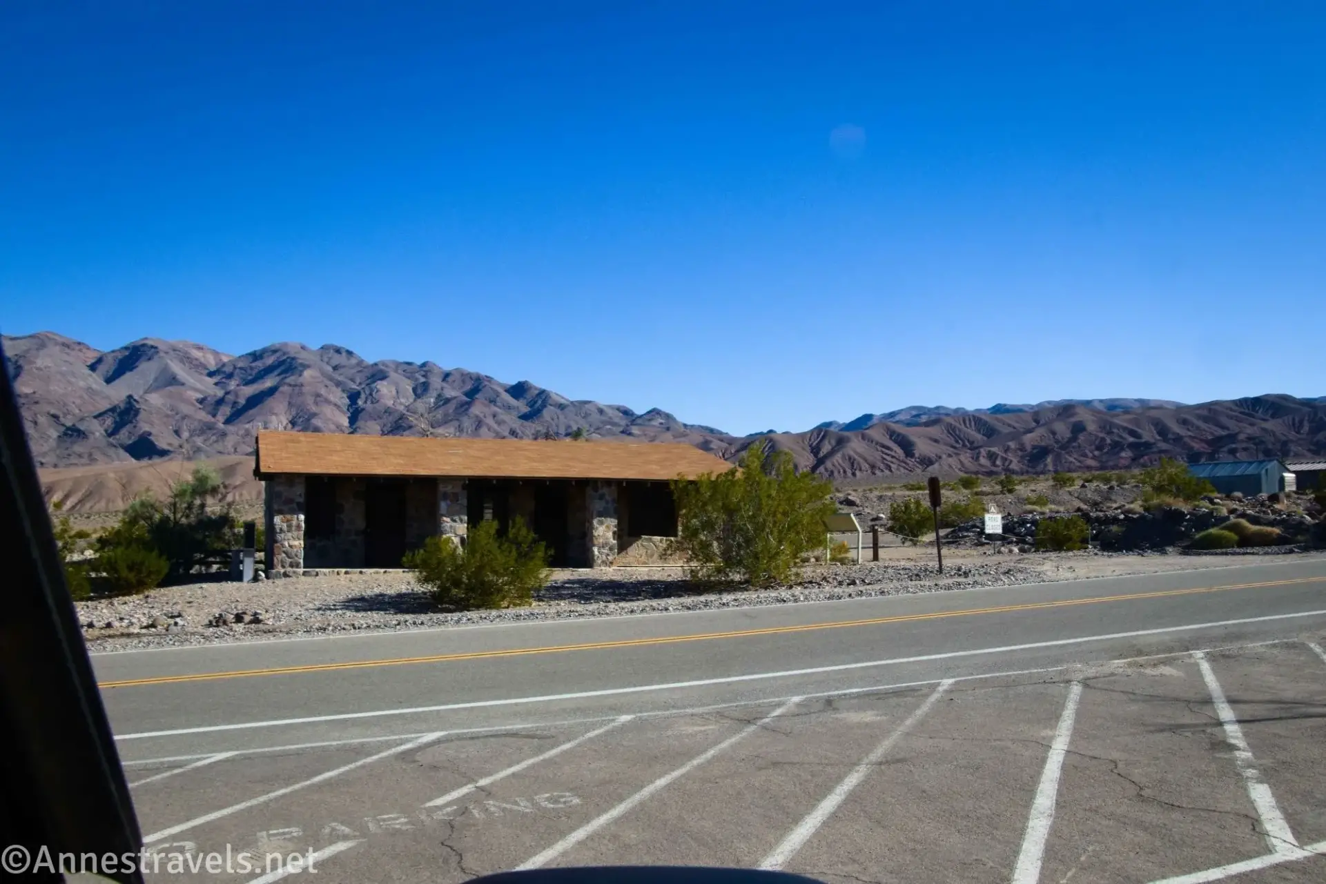 A stone building across the road with dry mountains beyond