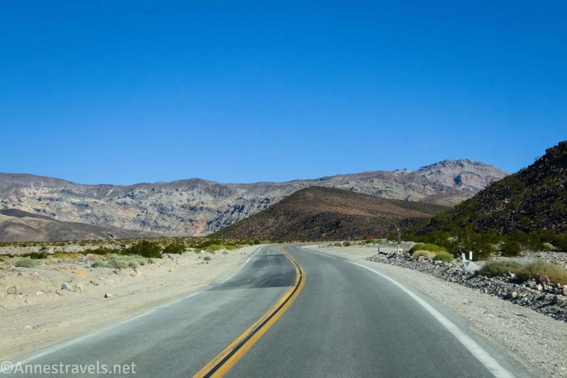 A blacktop road in a desert with dry mountains