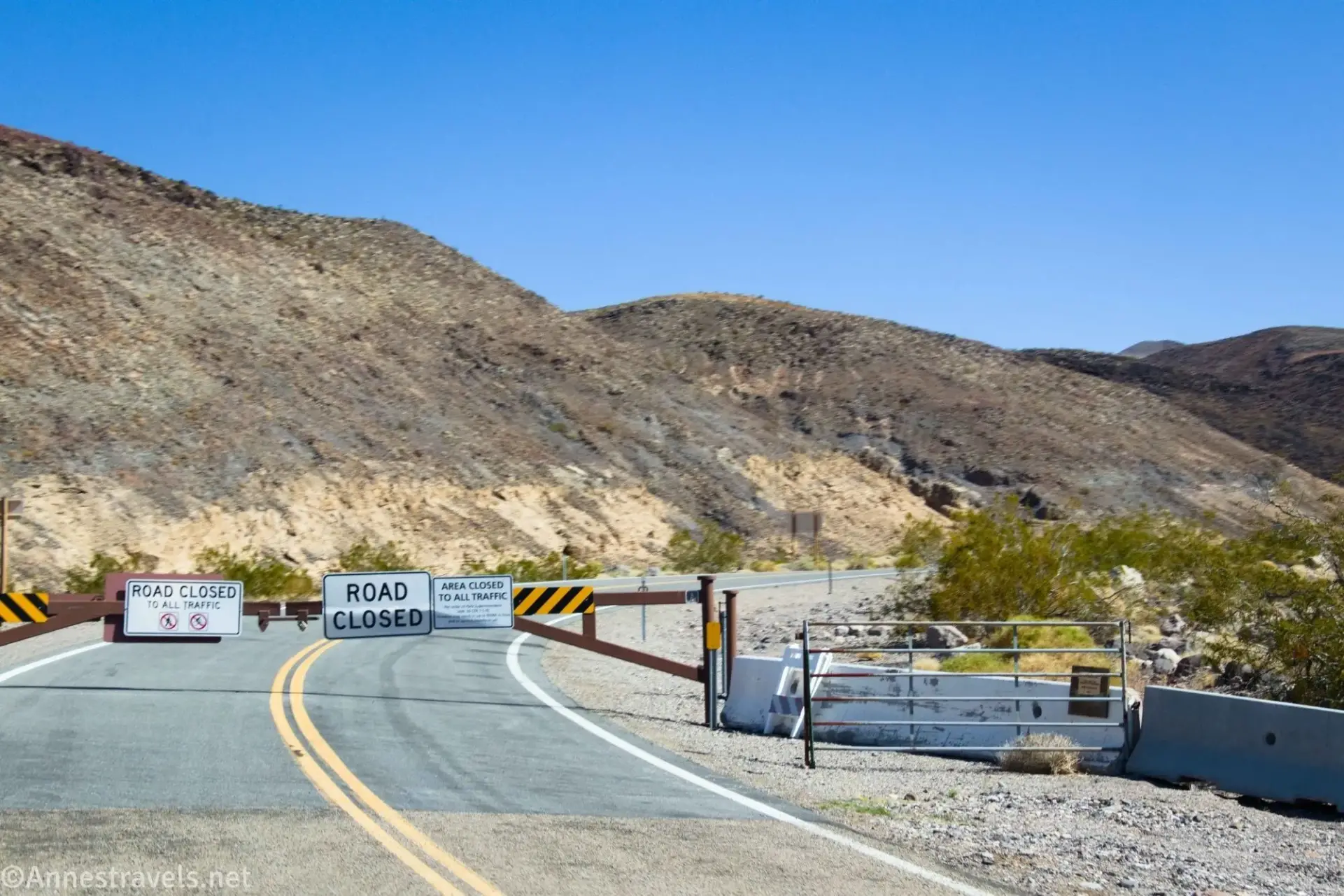 A gate closes the road with brown desert hills beyond
