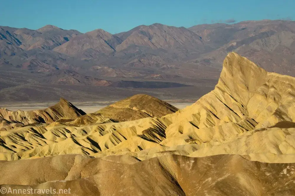 The trianular badland peak known as Manly Beacon surrounded by yellow badlands and gray mountains in Death Valley National Park