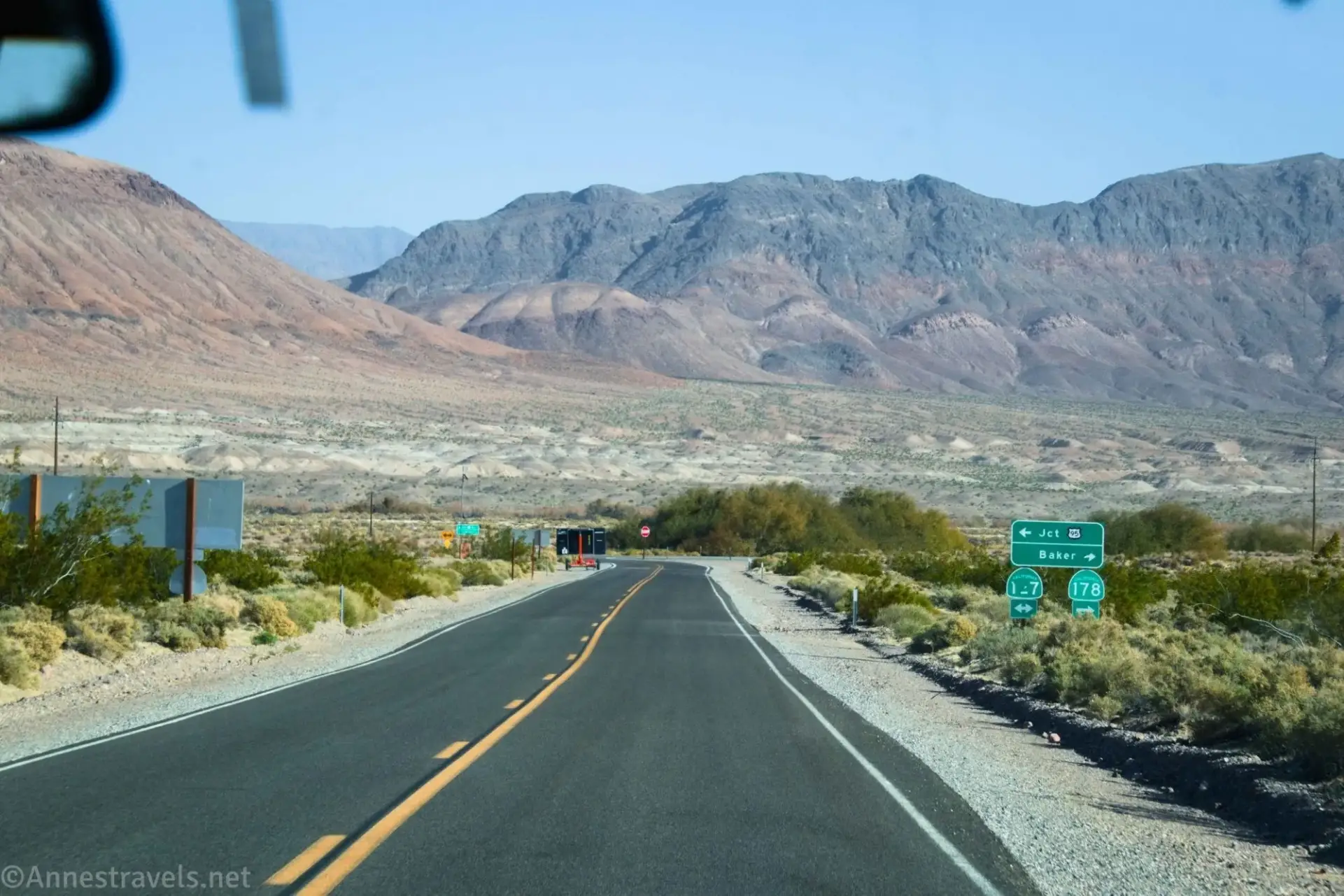 A paved road and signs below desert mountains
