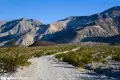 A gravel road twists between desert brush toward desert mountains and a brown hill