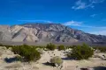 Cottonwood Mountains Brush on a desert plain with striped desert mountains below a few clouds in a blue sky