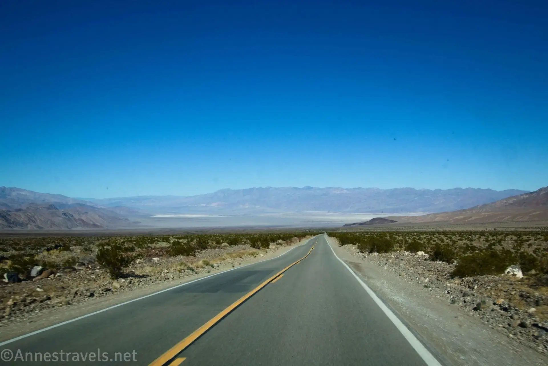 A blacktop road leading downhill through the desert into a valley