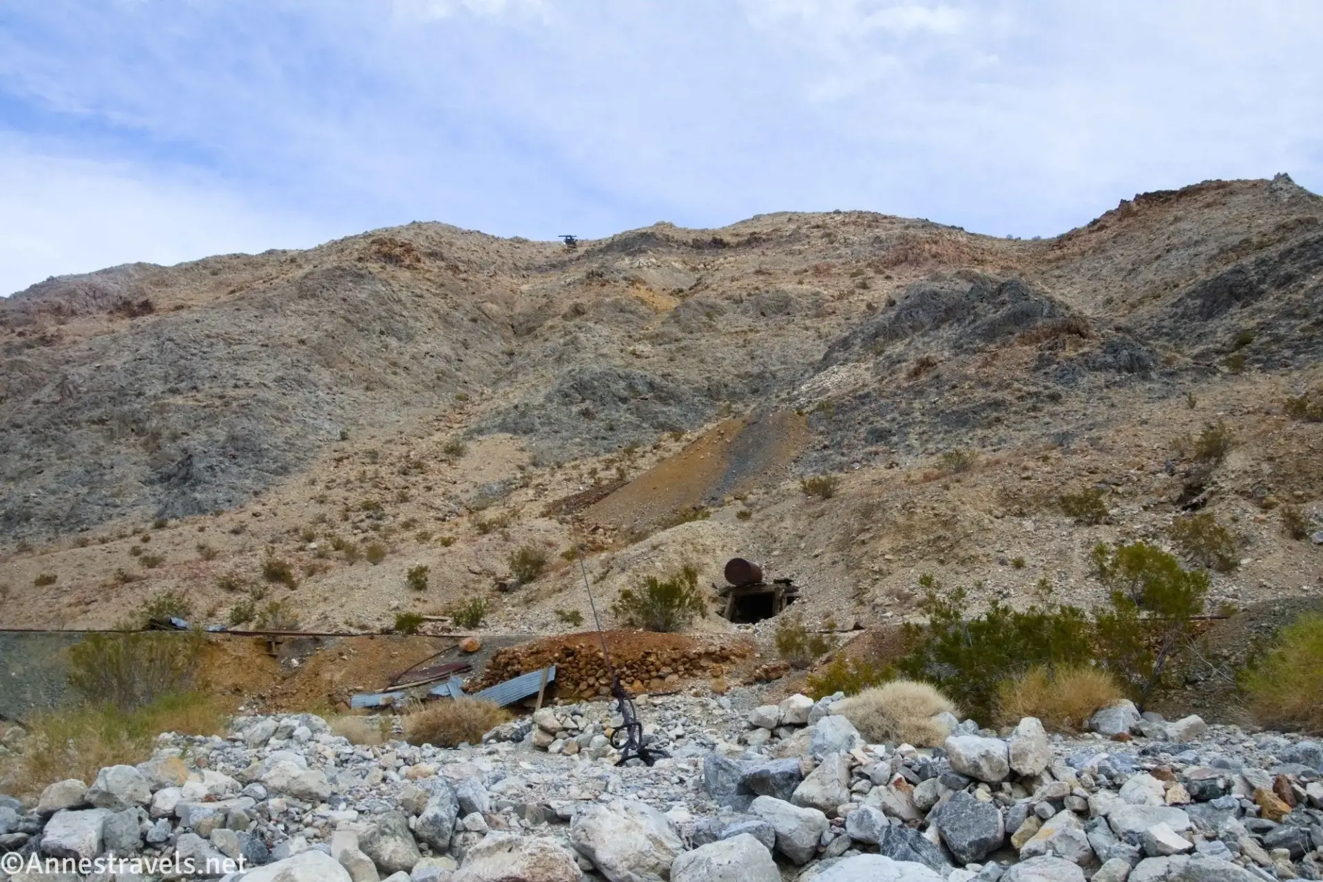 Rocks in front of old mining equipment, including a wire of a tramway reaching up a brown and gray hillside
