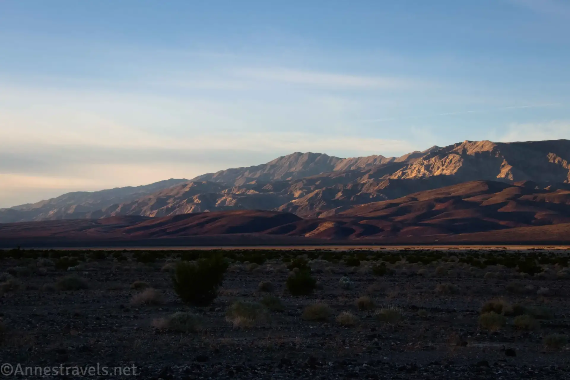 The glow of early morning sun on desert mountains across a shadowy plain