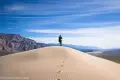 Walking on the Panamint Dunes Footprints on a rippled sand dune lead to a hiker in a green jacket with distant mountains and a desert valley