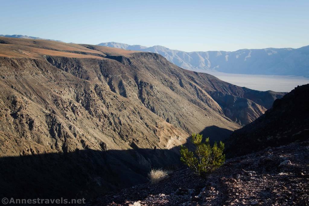 A desert canyon leads out to a hazy valley with distant mountains