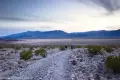 Two hikers on a dirt and gravel road above a desert plain and below dark clouds