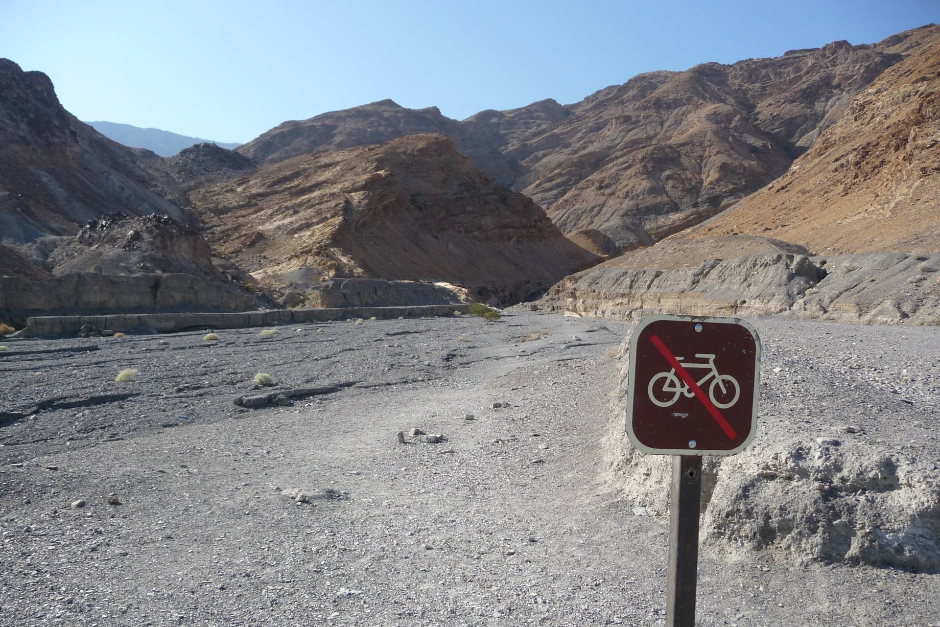 A no bicycles sign in a gravel wash near brown and gray mountains