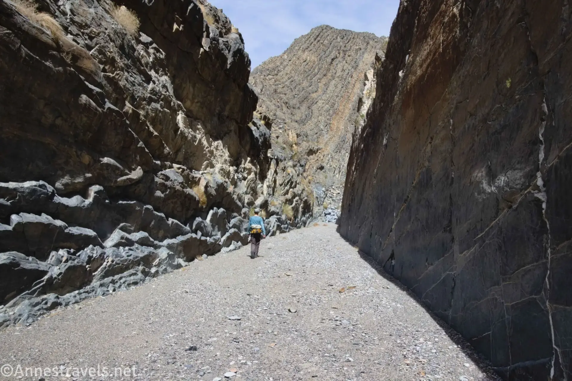 A hiker walks up a straight canyon with unique rock layer mountain at the end