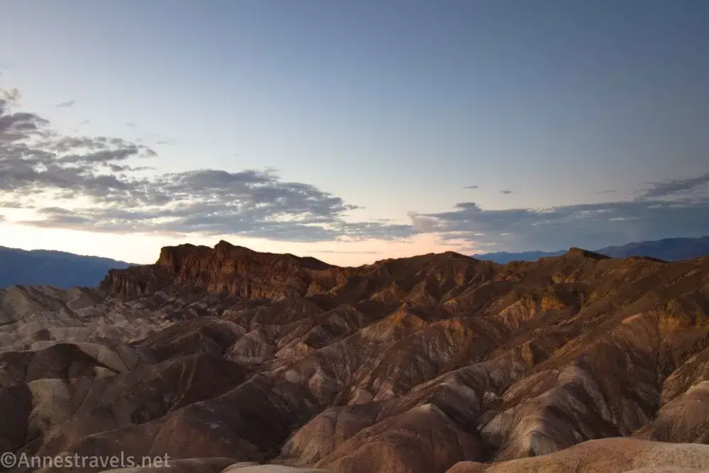 Muted red and striped badlands below sunset skies from Zabriskie Point in Death Valley National Park
