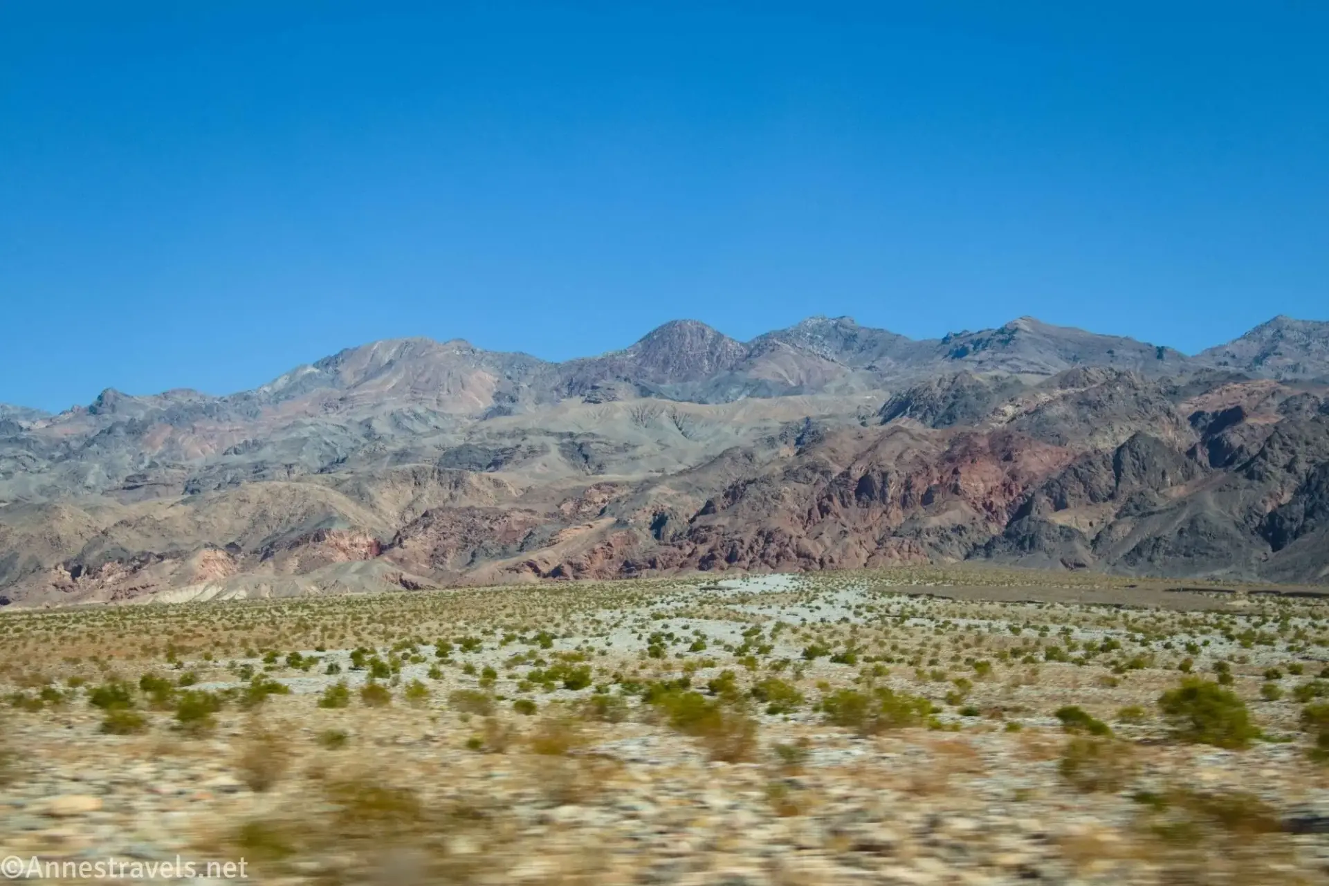 Red, black, and brown Grapevine Mountains above an alluvial fan with greasebushes