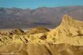 The trianular badland peak known as Manly Beacon surrounded by yellow badlands and gray mountains in Death Valley National Park