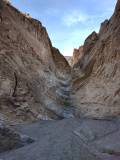 Dryfall in tan cliffs above a gravel wash and below a blue sky with clouds