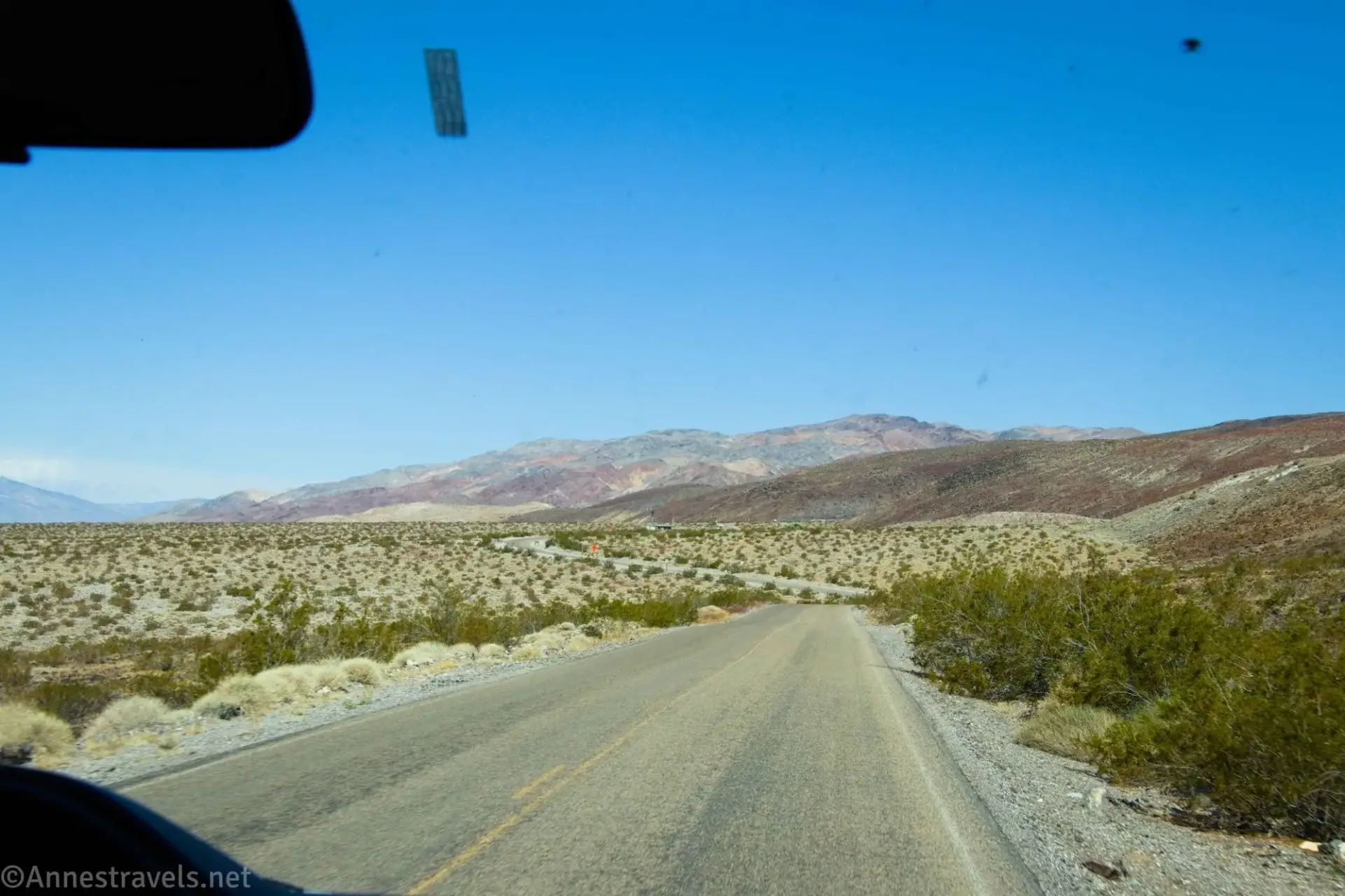 A dusty paved road curves as it travels across the desert toward colorful desert hills