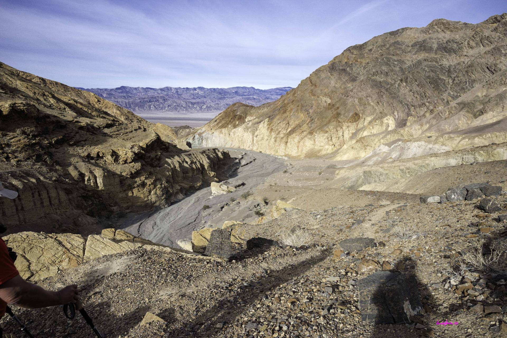 The shadow of a hiker on a gravel surface looking down into a desert canyon with distant mountains